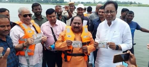 Officials in orange life jackets at a riverside, holding papers