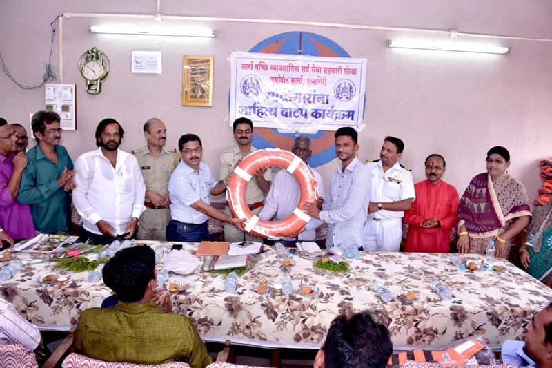 Officials and fishermen at a table, a lifebuoy being handed over, under a co-operative society banner