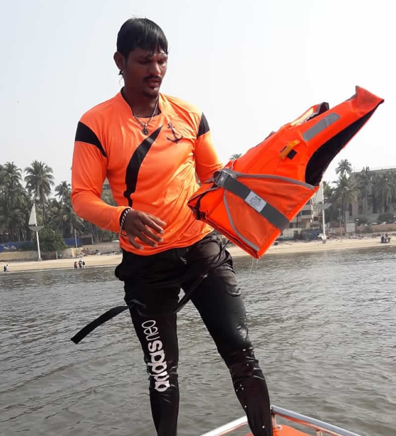 A lifeguard holding an MM life jacket, stepping aboard a boat near the shore