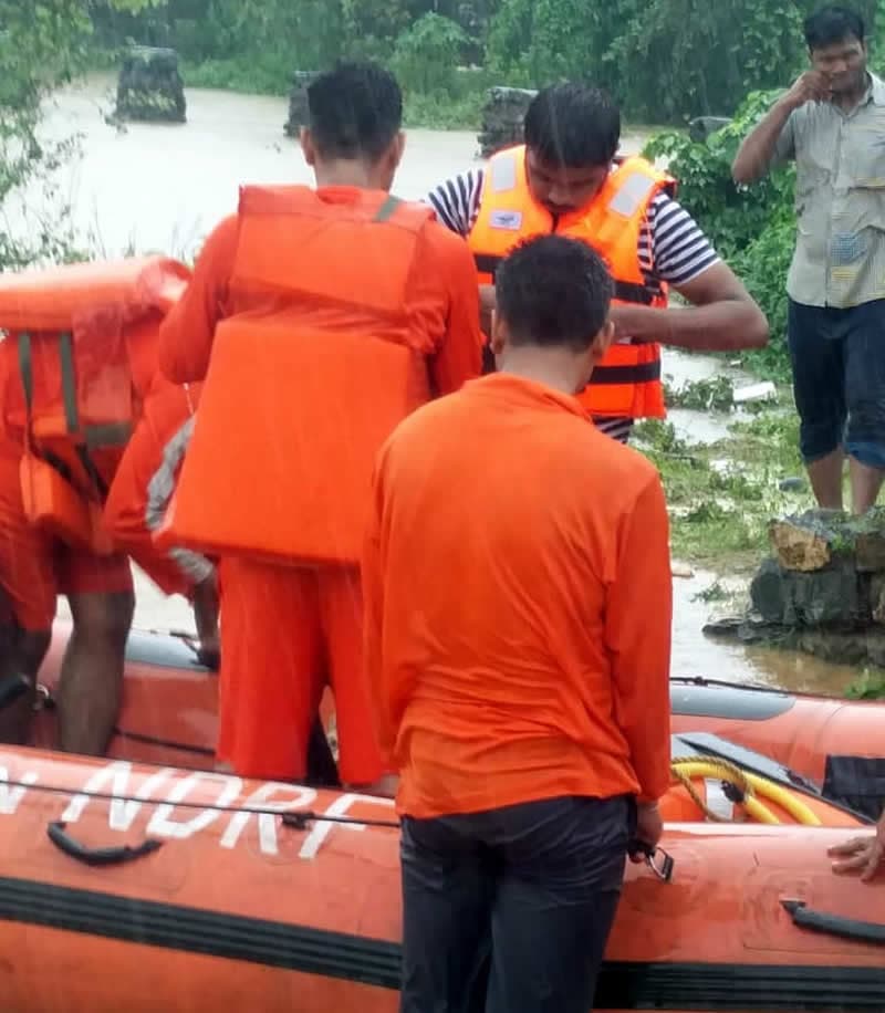 Rescuers in orange life jackets boarding an NDRF inflatable boat in floodwater